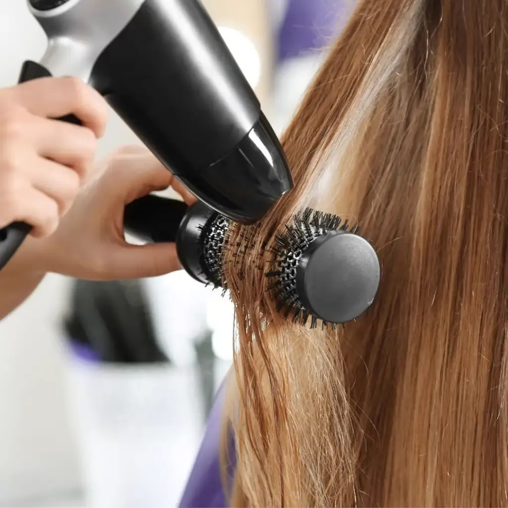 A stylist finishing hair with a round brush and dryer